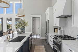 Kitchen with high end appliances, hanging light fixtures, sink, custom exhaust hood, and dark hardwood / wood-style floors