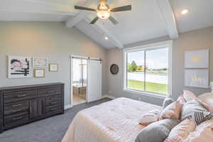 Bedroom featuring lofted ceiling with beams, baseboards, a barn door, dark carpet, and ensuite bathroom