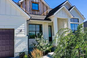 Property entrance with board and batten siding, a garage, and a shingled roof