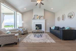 Living area featuring a large fireplace, baseboards, wood finished floors, a ceiling fan, and vaulted ceiling with beams