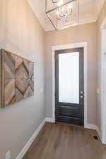 Foyer featuring crown molding, an inviting chandelier, baseboards, visible vents, and wood finished floors
