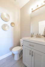 Half bath with baseboards, wood finished floors, toilet, and vanity