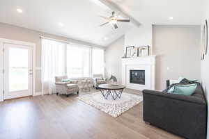 Living area featuring vaulted ceiling with beams, wood finished floors, a large fireplace, baseboards, and ceiling fan