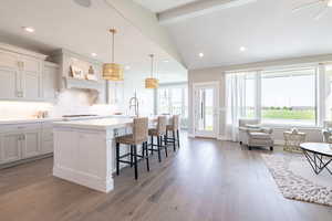 Kitchen with backsplash, vaulted ceiling with beams, a kitchen breakfast bar, a center island with sink, and light wood-type flooring