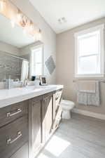 Bathroom featuring toilet, vanity, curtained shower, and visible vents