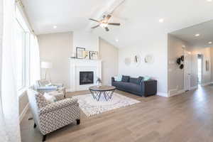 Living room with lofted ceiling with beams, wood finished floors, a large fireplace, visible vents, and ceiling fan