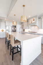 Kitchen with decorative backsplash, light countertops, light wood-style flooring, stainless steel appliances, and a spacious island