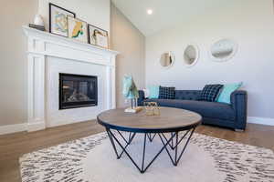 Living area featuring lofted ceiling, recessed lighting, baseboards, a fireplace, and wood finished floors