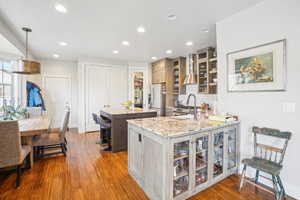 Kitchen with wood-type flooring, stainless steel refrigerator with ice dispenser, a kitchen island, light stone countertops, and pendant lighting