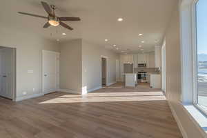 Unfurnished living room featuring ceiling fan, plenty of natural light, sink, and light wood-type flooring