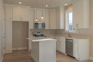 Kitchen with appliances with stainless steel finishes, pendant lighting, white cabinetry, sink, and a center island