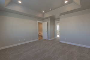 Unfurnished bedroom featuring a raised ceiling and carpet floors