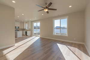 Unfurnished living room featuring a water view, ceiling fan, sink, and light hardwood / wood-style flooring