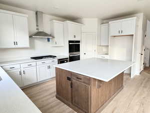 Kitchen featuring a center island, stainless steel double oven, wall chimney range hood, gas stovetop, and light wood-type flooring