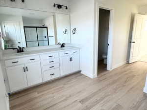 Bathroom featuring hardwood / wood-style floors, vanity, toilet, and a shower with door