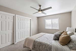 Bedroom with ceiling fan, light colored carpet, and two closets