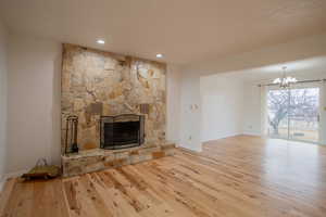 Unfurnished living room with a stone fireplace, a chandelier, and light hardwood / wood-style flooring