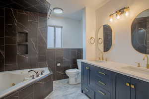 Bathroom featuring tile walls, vanity, toilet, tiled tub, and a textured ceiling