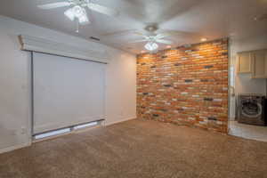 Carpeted empty room with brick wall, ceiling fan, washer / dryer, and a textured ceiling