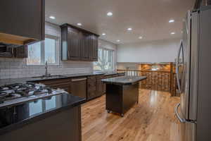 Kitchen featuring sink, a center island, light hardwood / wood-style flooring, dark stone countertops, and appliances with stainless steel finishes