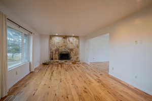 Unfurnished living room featuring a stone fireplace and light hardwood / wood-style floors