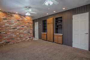 Unfurnished living room featuring ceiling fan, brick wall, light carpet, and a textured ceiling