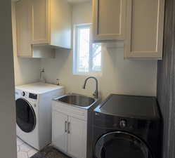 Clothes washing area featuring cabinets, separate washer and dryer, and sink