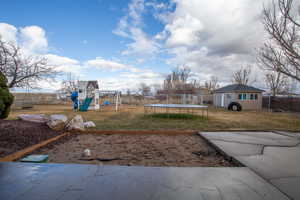 View of yard featuring a trampoline, an outdoor structure, and a playground