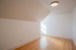 Additional living space with vaulted ceiling, light wood-type flooring, and a textured ceiling