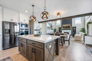 Kitchen featuring a center island, quartz countertops, white cabinetry, appliances with stainless steel finishes, and decorative light fixtures, beamed ceiling