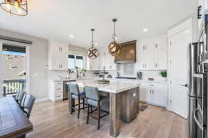 Kitchen with white cabinets, hanging light fixtures, stainless steel appliances, and a kitchen island