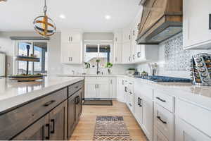 Kitchen featuring stainless steel gas cooktop, quartz countertops tasteful backsplash, custom range hood, white cabinetry