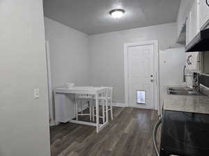 Kitchen featuring a textured ceiling, range, sink, white cabinets, and dark wood-type flooring