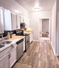 Kitchen with sink, appliances with stainless steel finishes, light hardwood / wood-style floors, a textured ceiling, and white cabinets