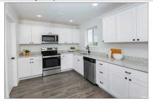 Kitchen featuring light stone countertops, sink, dark wood-type flooring, stainless steel appliances, and white cabinets