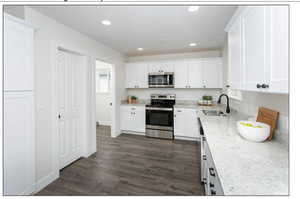 Kitchen with light stone counters, sink, white cabinetry, and stainless steel appliances