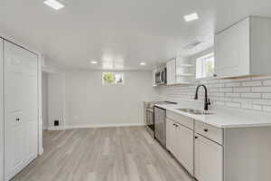 Kitchen with sink, appliances with stainless steel finishes, white cabinets, light wood-type flooring, and decorative backsplash