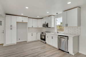 Kitchen featuring light hardwood / wood-style floors, stainless steel appliances, white cabinets, hanging light fixtures, and sink