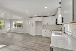 Kitchen with light hardwood / wood-style floors, white cabinetry, sink, light stone countertops, and backsplash