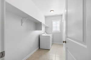 Clothes washing area featuring light tile patterned floors, visible vents, washing machine and dryer, laundry area, and baseboards