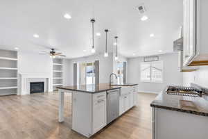 Kitchen with an island with sink, appliances with stainless steel finishes, dark stone countertops, decorative light fixtures, and white cabinetry