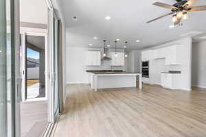 Kitchen with white cabinets, appliances with stainless steel finishes, decorative light fixtures, a kitchen island with sink, and wall chimney range hood