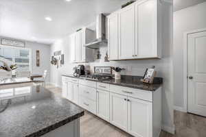 Kitchen with white cabinetry, wall chimney range hood, and light hardwood / wood-style flooring