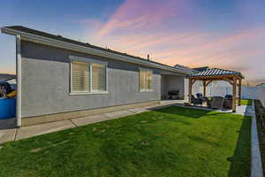 Back house at dusk featuring a patio area, a lawn, a gazebo, and an outdoor living space