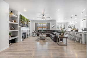 Living room featuring light wood-type flooring, built in features, ceiling fan, and a tile fireplace