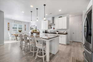 Kitchen featuring white cabinets, wall chimney range hood, and a kitchen island with sink