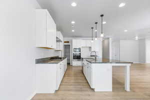 Kitchen featuring decorative light fixtures, stainless steel appliances, white cabinets, a sink, and an island with sink