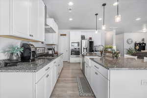 Kitchen featuring stainless steel appliances, white cabinets, sink, pendant lighting, and light hardwood / wood-style flooring