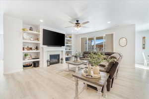 Living room featuring a fireplace, ceiling fan, built in features, and light wood-type flooring