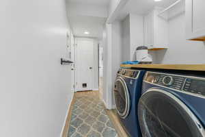 Laundry room featuring light wood-type flooring, washing machine and dryer, and cabinets